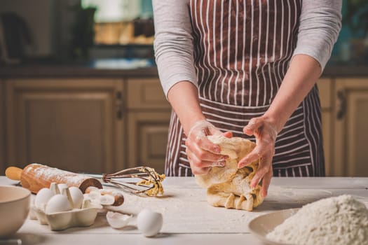 Woman hands kneading dough on kitchen table. A woman in a striped apron is cooking in the kitchen