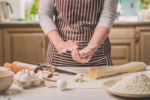 Woman bake pies. Confectioner makes desserts. Making buns. Dough on the table. Knead the dough. A woman in a striped apron is cooking in the kitchen