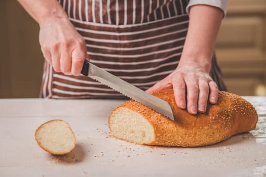 Woman cutting bread on wooden board. Bakehouse. Bread production. A woman in a striped apron