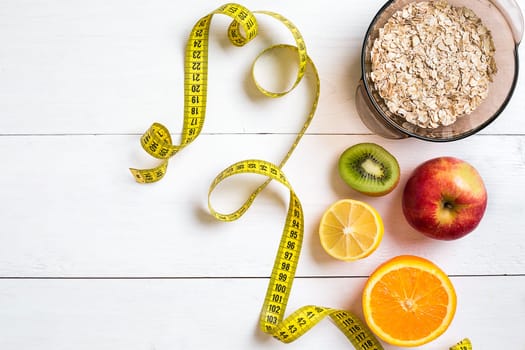 Fitness concept with fruit, bowl of oatmeal and centimeter. Top view background concept. Copy space