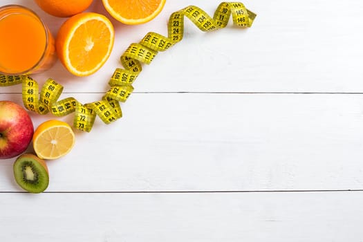 Fresh fruits with tape measure over white wooden background. Fitness concept. Top view. Copy space Flat lay