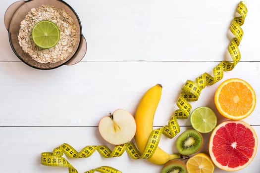 Fresh fruits with tape measure over white wooden background. Fitness concept. Top view. Copy space Flat lay
