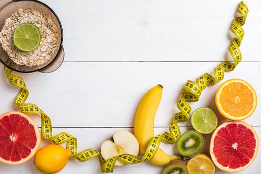 Fresh fruits with tape measure over white wooden background. Fitness concept. Top view. Copy space Flat lay