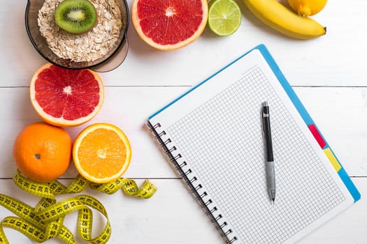 Healthy breakfast with oatmeal, fresh fruits and notebook on rustic wooden table. Top view.
