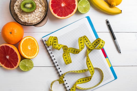 Healthy breakfast with oatmeal, fresh fruits and notebook on rustic wooden table. Top view.