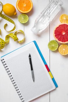 Healthy breakfast with fresh fruits and bottle of water with notebook on rustic wooden table. Top view.