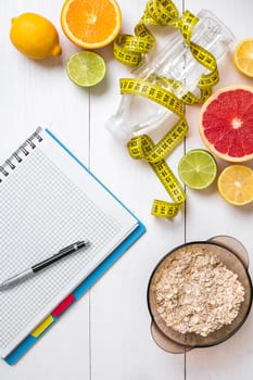 Healthy breakfast with oatmeal, fresh fruits and bottle of water with notebook on rustic wooden table. Top view.