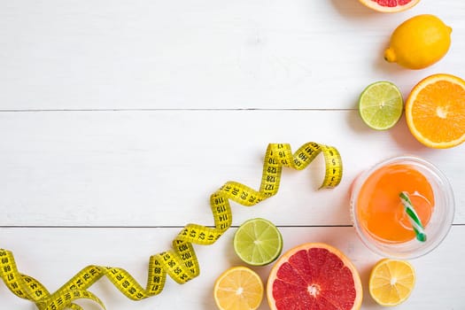 Fresh fruits with tape measure over white wooden background. Fitness concept. Flat lay. Top view. Copy space