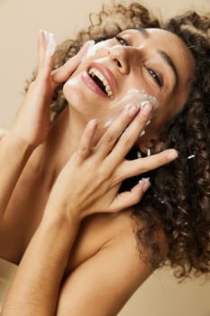 Woman beauty face close-up applying foam to wash and cleanse skin with fingers of her hand, nail and hair health, hair dryer style curly afro hair, body and beauty care concept. High quality photo