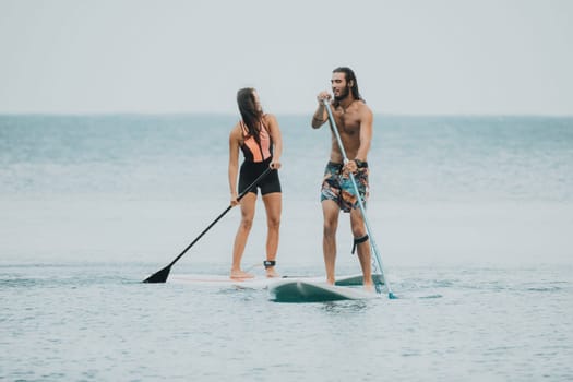 Sea woman and man on sup. Silhouette of happy young woman and man, surfing on SUP board, confident paddling through water surface. Idyllic sunset. Active lifestyle at sea or river