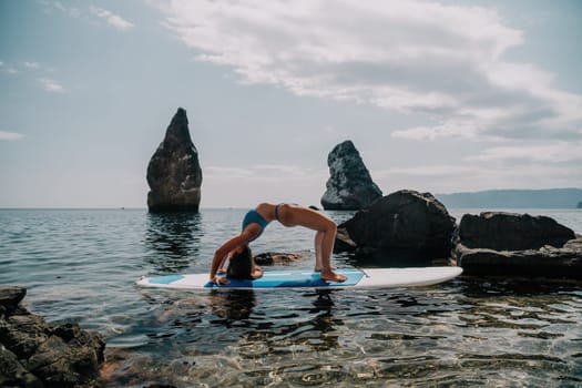 Woman sup yoga. Middle age sporty woman practising yoga pilates on paddle sup surfboard. Female stretching doing workout on sea water. Modern individual hipster outdoor summer sport activity