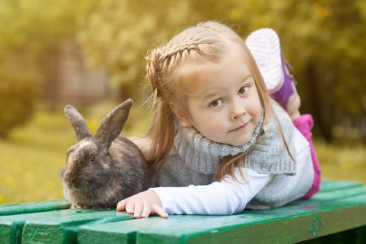 Cute brown-eyed girl lying on bench with rabbit, close-up