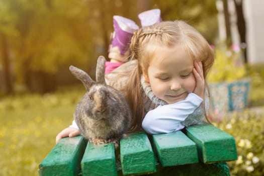Adorable girl posing on bench with cute rabbit, close-up