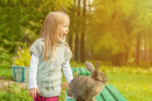 Cheerful little girl walking with rabbit in park, close-up
