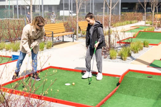 mother and daughter enjoying together playing mini golf in the city