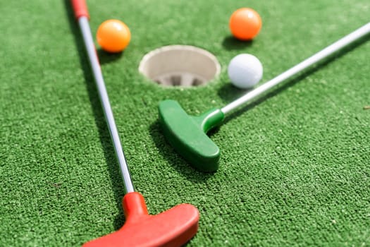 Close-up of miniature golf hole with bat and ball.