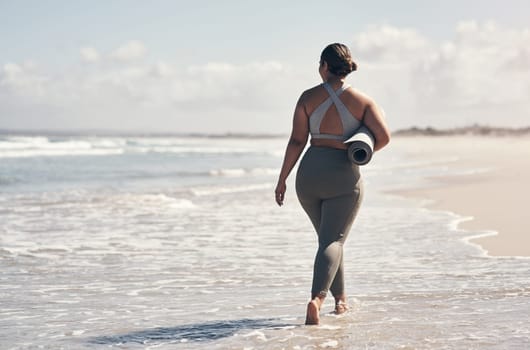 Yoga has taught me to be kind to myself. Rearview shot of a woman walking on the beach with her yoga mat