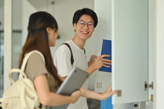 Two young college friends talking while standing at lockers in campus hallway. Education, Learning and technology concept.