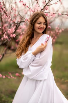 Woman peach blossom. Happy curly woman in white dress walking in the garden of blossoming peach trees in spring.