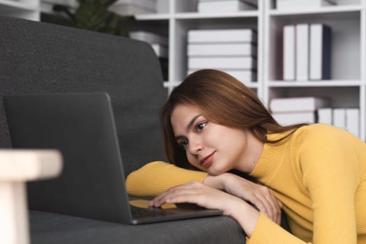 Image of cheerful asian woman in laying on sofa using laptop..