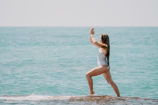 Woman sea yoga. Back view of free calm happy satisfied woman with long hair standing on top rock with yoga position against of sky by the sea. Healthy lifestyle outdoors in nature, fitness concept.