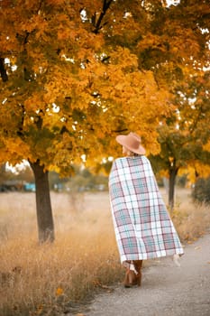 autumn woman in a brown hat, plaid, against the background of an autumn tree.