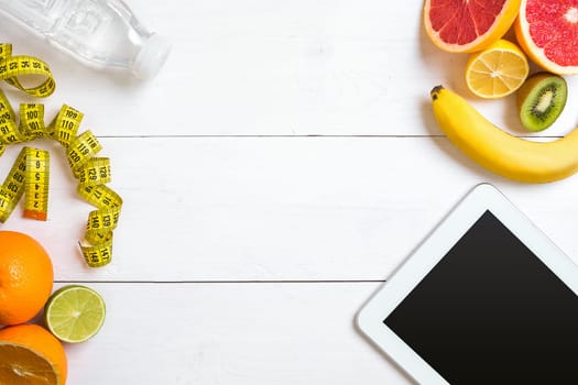 Healthy breakfast with oatmeal, fresh fruits and bottle of water with tablet on rustic wooden table. Top view.