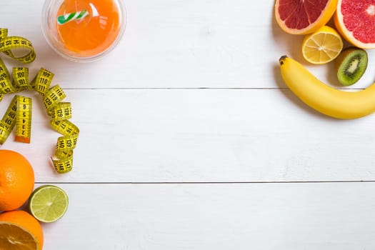 Fresh fruits with tape measure over white wooden background. Fitness concept. Top view. Copy space Flat lay