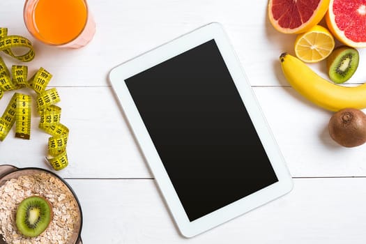 Fresh juice in glass from citrus fruits - lemon, grapefruit, orange, bowl of oatmeal on white wooden background, top view. White tablet with copy space