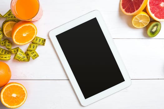 Fresh juice in glass from citrus fruits - lemon, grapefruit, orange on white wooden background, top view. White tablet with copy space