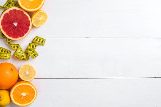 Fresh fruits with tape measure over white wooden background. Fitness concept. Flat lay. Top view. Copy space