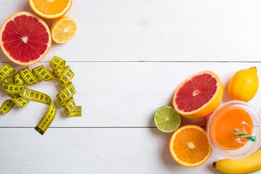 Fresh fruits with tape measure over white wooden background. Fitness concept. Top view. Copy space Flat lay