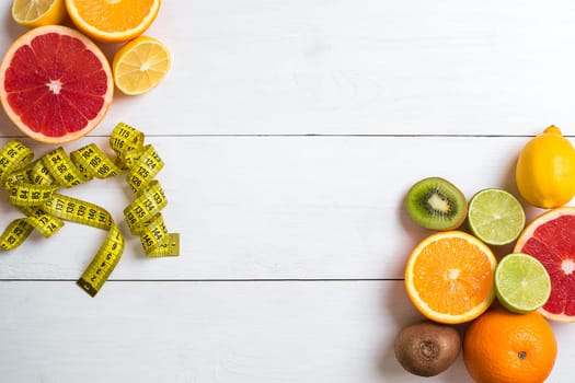 Fresh fruits with tape measure over white wooden background. Fitness concept. Top view. Copy space Flat lay
