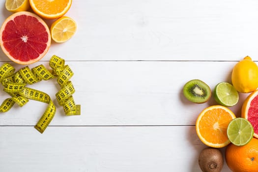 Fresh fruits with tape measure over white wooden background. Fitness concept. Top view. Copy space Flat lay