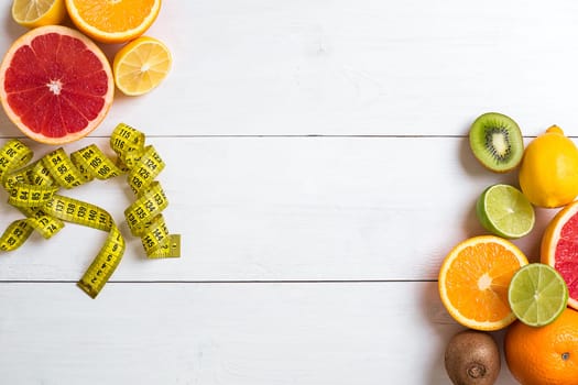 Fresh fruits with tape measure over white wooden background. Fitness concept. Top view. Copy space Flat lay