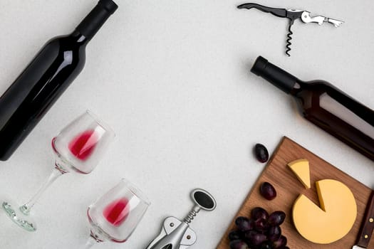 Two glasses of red wine, cheese and grapes. Two bottles of wine and a corkscrew. Top view with copy space