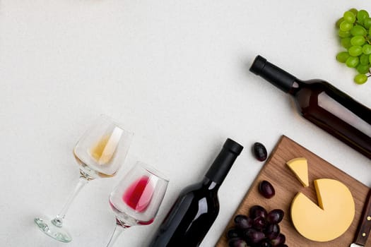 Two wine glasses with red and white wine,bottles of red wine and white wine, cheese on white background. Horizontal view from the top. Mock-up. Copy space. Flat lay