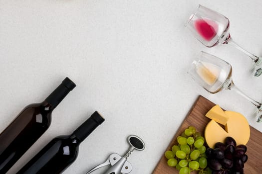 Two glasses of white and red wine, cheese and grapes. Two bottles of wine and a corkscrew. Top view with copy space
