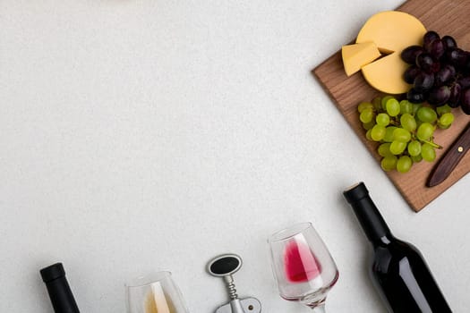 Two glasses of white and red wine, cheese and grapes. Two bottles of wine and a corkscrew. Top view with copy space
