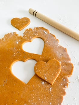 The process of cooking heart cookies. Top view of raw dough, rolling pin and baking cutter