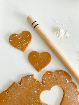 The process of cooking heart cookies. Top view of raw dough, rolling pin and baking cutter