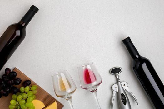 Two glasses of white and red wine, cheese and grapes. Two bottles of wine and a corkscrew. Top view with copy space