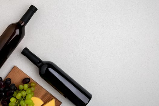 Two bottles of white and red wine, cheese and grapes. Top view with copy space