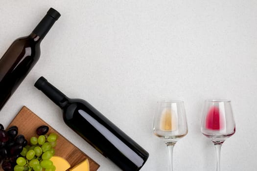 Two glasses of white and red wine, cheese and grapes. Two bottles of wine. Top view with copy space