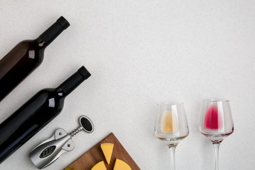 Two glasses of white and red wine and cheese. Two bottles of wine and a corkscrew. Top view with copy space
