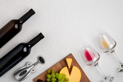 Two glasses of white and red wine, cheese and grapes. Two bottles of wine and a corkscrew. Top view with copy space