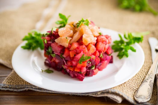 vinaigrette salad of boiled vegetables with salted fish in a plate, on a wooden table.