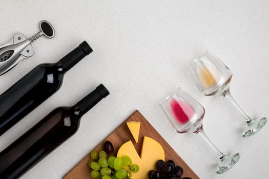 Two glasses of white and red wine, cheese and grapes. Two bottles of wine. Top view with copy space