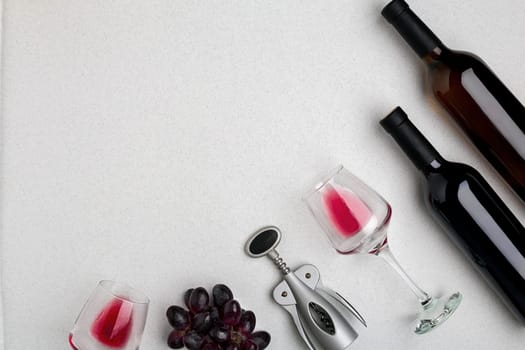 Two glasses of red wine and grapes. Two bottles of wine and a corkscrew. Top view with copy space