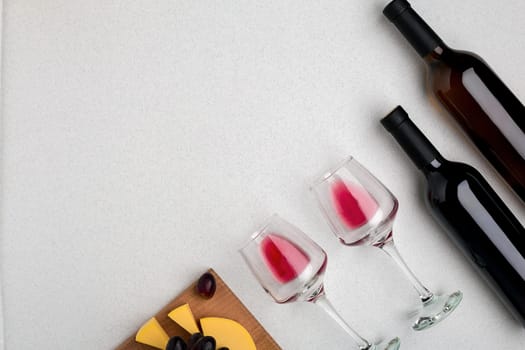 Two glasses of red wine, cheese and grapes. Two bottles of wine and a corkscrew. Top view with copy space